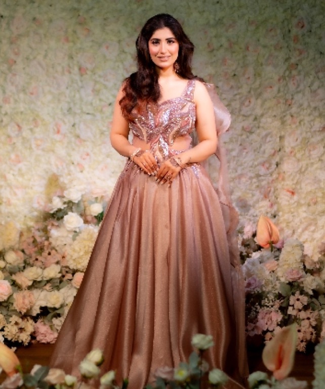 Woman in a rose-gold gown in front of a floral wall